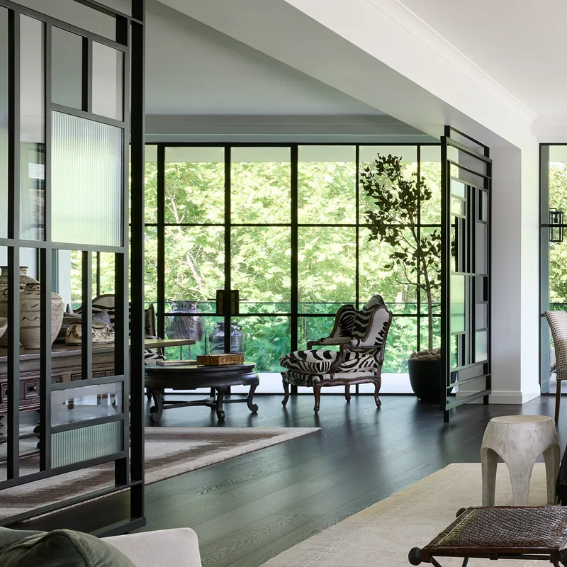 Black steel windows and glazed partitions frame a light-filled living room at Brivana Residence.