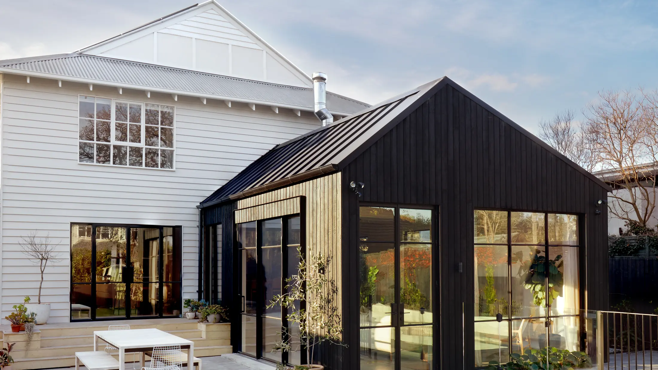 Black steel-framed windows and glazed doors on a dark-clad extension beside a white weatherboard residence in Yarraville.