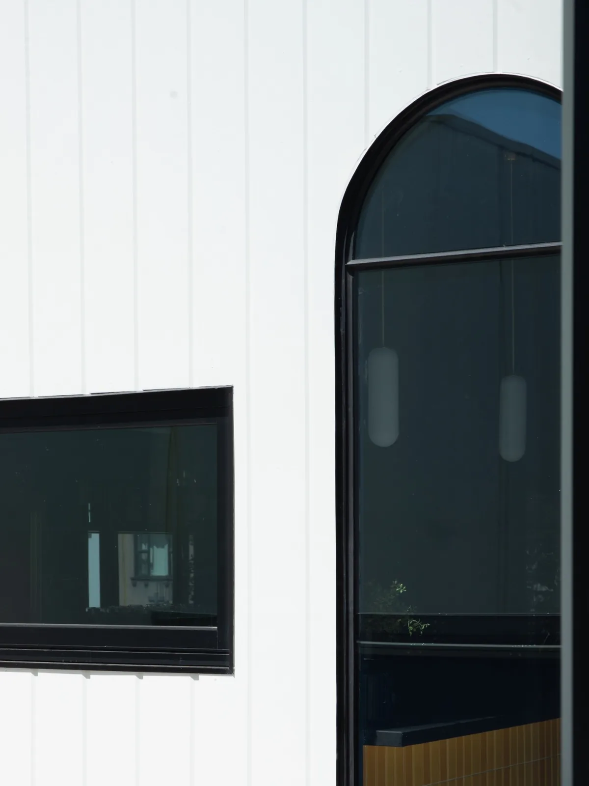 Black arched and rectangular steel windows against white vertical cladding at DUX Albury.