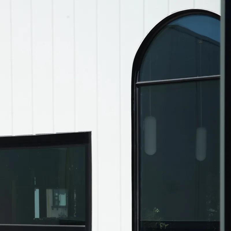 Close-up of an arched black steel window beside a rectangular window on DUX Albury’s white façade.