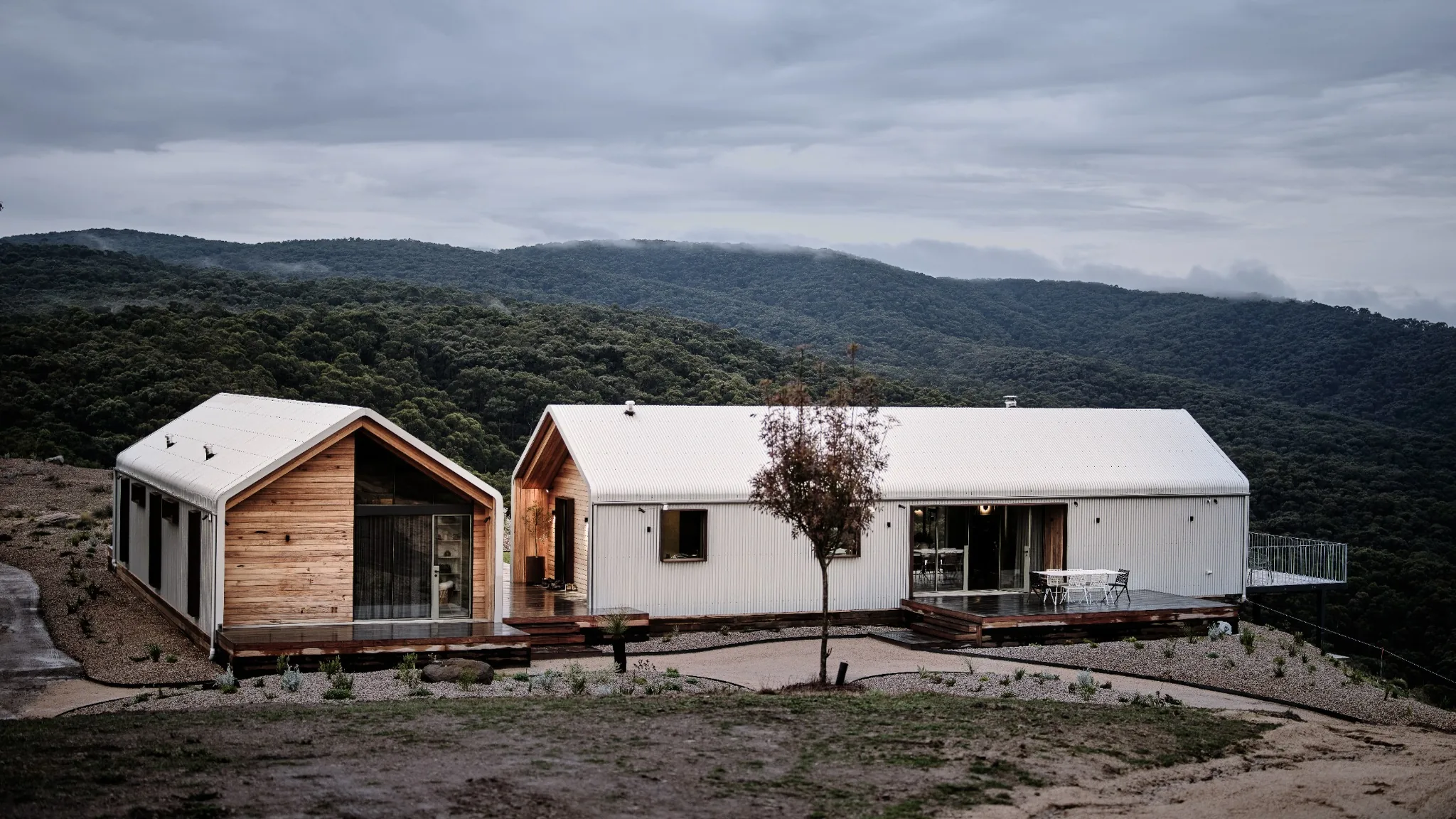 Strath Creek Farm House with steel-framed glazing, timber and white cladding, pitched roofs and decks against wooded hills.